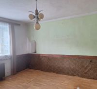 Interior of a family house with a green wall, wood-patterned flooring, and curtains.