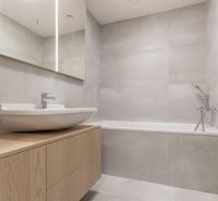 Bathroom with a bathtub, a sink on a wooden cabinet, a mirror, and light tiles in a studio apartment.