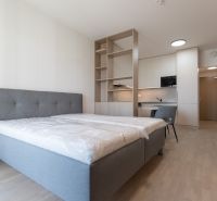A one-bedroom apartment's bedroom with a bed, kitchenette, and wooden decor flooring.
