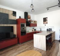 Living room in a two-room apartment with a red kitchen unit and a wooden decor floor.