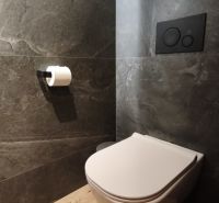A bathroom with a wall-mounted toilet and a floor with a wood decor in a 2-room apartment.