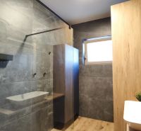 A bathroom with dark tiles, a shower corner, and a floor with a wooden decor in a 2-room apartment.