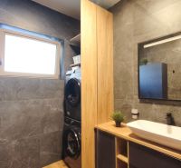 A bathroom in a 2-room apartment with dark tiles and a washer with a dryer.