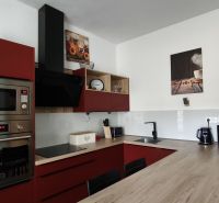A kitchen with red cabinets and appliances in a 2-room apartment with a wood-patterned floor.