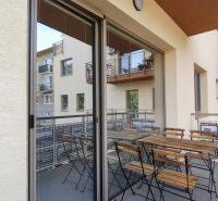 A balcony with seating in a 2-room apartment with a view of neighboring buildings.
