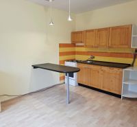 A kitchen in a one-room apartment with a wooden decor floor, wooden cabinets, and orange tiles.