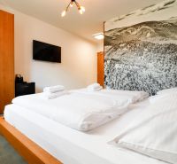 Bedroom of a vacation apartment with a large bed, a picture of mountains, and a TV on the wall.