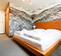 A bedroom in a holiday apartment with a wooden bed and a mountain photo wallpaper.