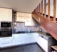 A kitchen in a 2-room apartment with stairs and appliances, with a wooden decor floor.