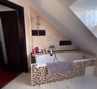 Bathroom with a bathtub in the attic of a 2-room apartment, light tiles, sloped roof.