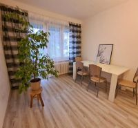 A room in a 2-room apartment with a dining table, chairs, and a floor with a wood decor.