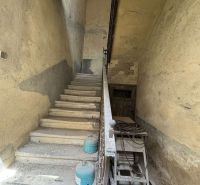 An old staircase in commercial premises with peeling walls and containers on the floor.
