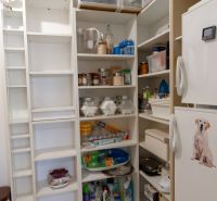 A storage room in a 3-room apartment with shelves full of groceries and a cooling box.