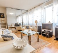A bright living room with a cream sofa, a glass table, and a wooden decor floor.
