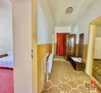 A hallway in a family house with carpets and retro furniture. On the left, a bedroom with red motifs.