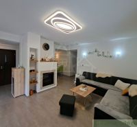 Living room with a fireplace, large sofa, and wood-patterned flooring in a family house.