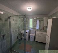 Bathroom in a family house with a washing machine, shower cabin, and green tiles.
