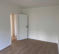 An empty room with white walls and a wood-patterned floor in a three-room apartment.