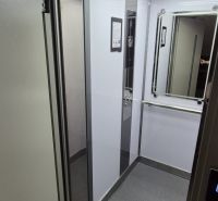 The interior of the elevator in a 3-room apartment building with lighting and a mirror.