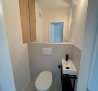 A bathroom in a 3-room apartment with a toilet, sink, and storage cabinets.