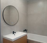 A bathroom with a round mirror and a wooden cabinet in a family house.
