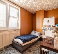 A room in a family house with a bed, a table, a radiator, and wooden paneling.