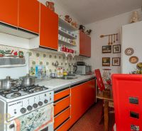 A kitchen in a family house with an orange cabinet, a stove, and decorative items on the walls.
