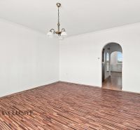 A spacious room in a 2-room apartment with a wooden decor floor and an arched passage.
