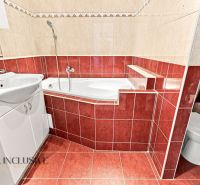 A bathroom with a bathtub and a sink in a 2-room apartment, tiled with red and beige tiles.