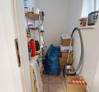 A pantry in a 3-room apartment with stored appliances, cardboard boxes, and a vacuum cleaner.