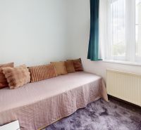 A room in a 3-room apartment with a sofa, cushions, and a table by the window.