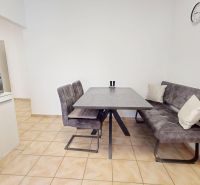 A kitchen in a 3-room apartment with a dining table, a gray bench, and a microwave oven.