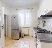 A kitchen with white cabinets and tiles in a 3-room apartment with a window and a refrigerator.