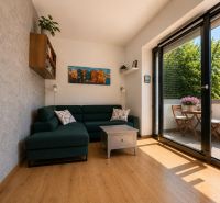 Living room in a two-room apartment with a green sofa, balcony, and wood-patterned flooring.
