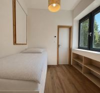 A simple room with a bed, a window, and a floor with a wooden decor in a two-room apartment.