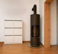 A wood-burning stove in a 2-room apartment on a floor with a wooden decor next to a white cabinet.