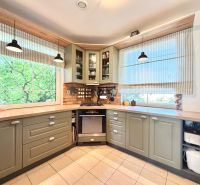 A kitchen in a family house with rustic cabinets and large windows, the lights complement the space.