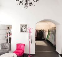 Black chandelier, pink armchair, coat rack, and dresses in commercial premises.