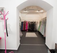 A retail space with racks full of evening dresses and a pink chair.