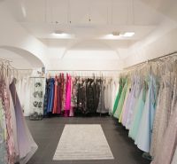 Retail space with colorful dresses, a showcase with jewelry, a carpet on a black floor.