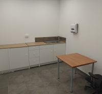 Commercial space with a kitchen unit, table, and gray flooring with a wooden decor.