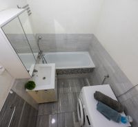 Bathroom with a shower and a washing machine in a 2-room apartment with tiles and a mirrored cabinet.