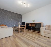 Living room in a two-room apartment with a wood-patterned floor, beige sofas, TV stand.