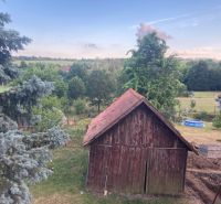 A garden view in the village of Volkovce with a wooden shed and trees.