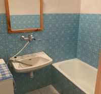 The bathroom in the three-room apartment has blue tiles, a bathtub, and a sink.