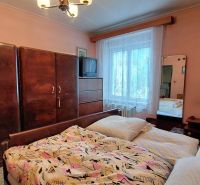Bedroom with wooden furniture and a TV in a two-room apartment, pink walls, bed linens.