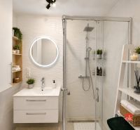 A bathroom in a studio apartment with a sink, shower, shelves, and a mirror.
