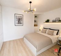 A bright bedroom with a bed, decor, a hanging lamp, and a wood-patterned floor in a studio apartment.