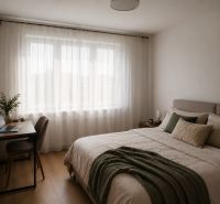 A bright bedroom in a two-room apartment with a wood-patterned floor, a desk, and a double bed.