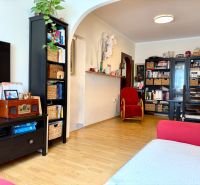 Living room with wood-patterned flooring, black furniture, and a bookshelf in a three-room apartment.